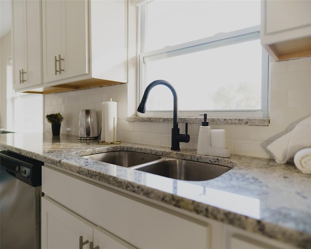 kitchen view of a sink, dishwasher, white cabinets, tasteful backsplash, and light stone counters