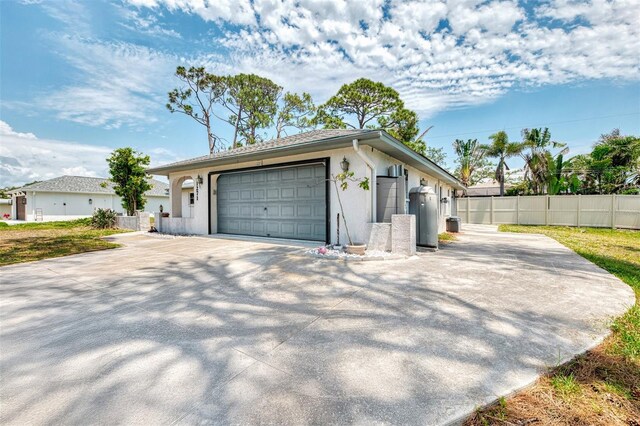 view of home's exterior with fence, driveway, a garage, stucco siding, and an outdoor structure