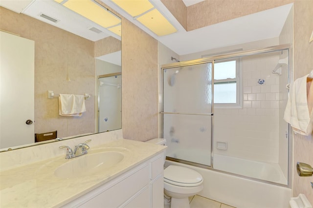 bathroom featuring toilet, vanity, bath / shower combo with glass door, and tile patterned flooring