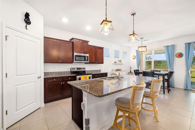 kitchen with appliances with stainless steel finishes, a sink, light tile patterned floors, a kitchen bar, and dark stone counters