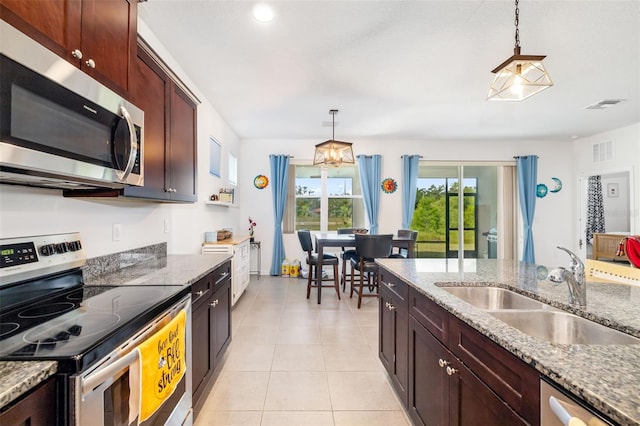 kitchen featuring stainless steel appliances, a sink, hanging light fixtures, light tile patterned floors, and stone countertops