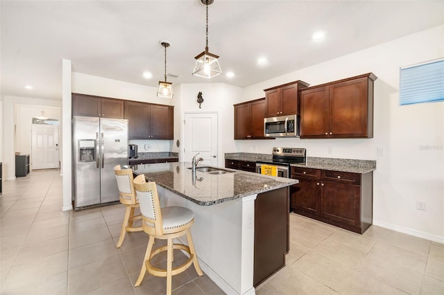 kitchen with stainless steel appliances, a sink, dark stone counters, recessed lighting, and an island with sink