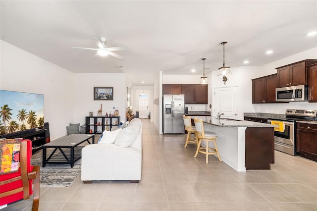 kitchen featuring appliances with stainless steel finishes, open floor plan, a ceiling fan, a kitchen bar, and light tile patterned flooring