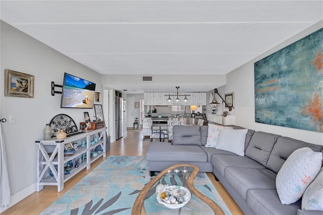 living room featuring light wood-style floors, a chandelier, and baseboards