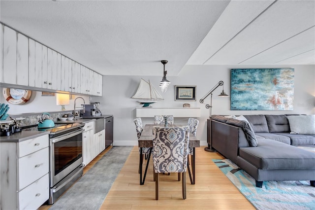 kitchen featuring stainless steel appliances, white cabinets, light wood finished floors, open floor plan, and a textured ceiling