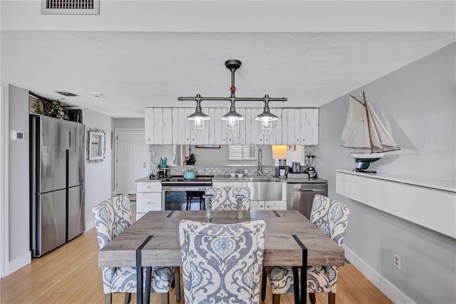 dining room with light wood finished floors, baseboards, and a textured ceiling