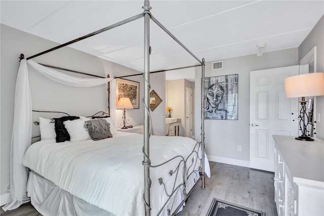 bedroom with wood finished floors, baseboards, and ensuite bathroom