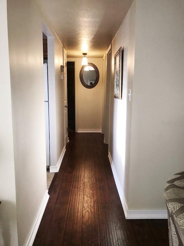 hallway featuring dark wood-type flooring and baseboards