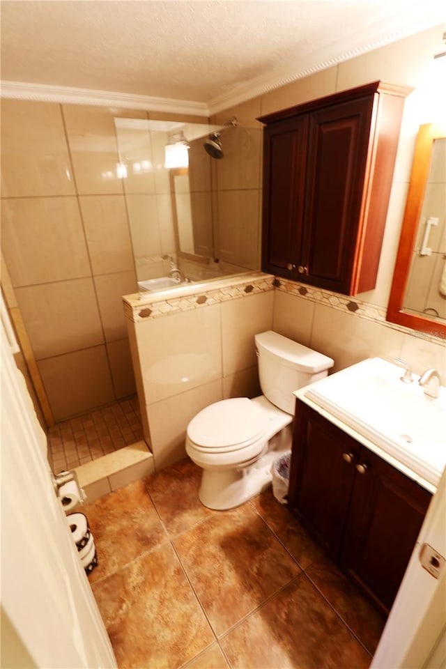 bathroom featuring toilet, tiled shower, tile walls, vanity, and ornamental molding