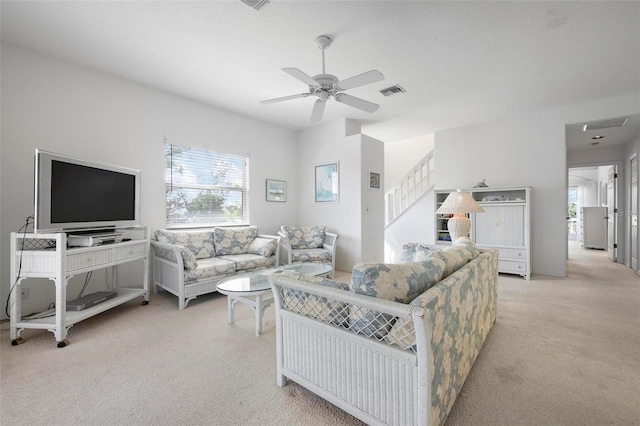 living area with light carpet, plenty of natural light, ceiling fan, and stairway