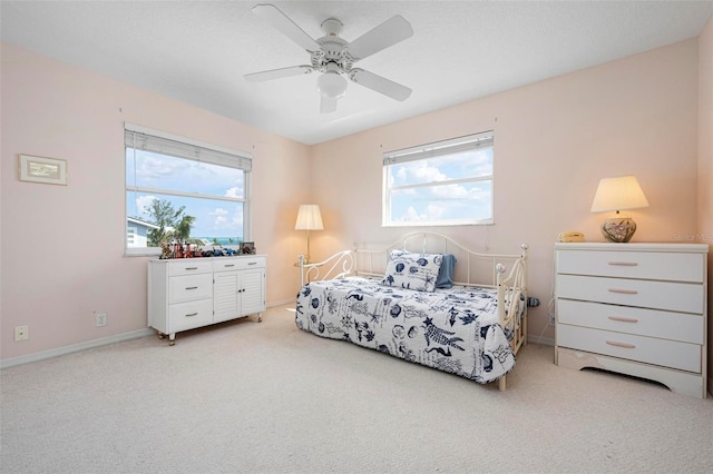 bedroom featuring light colored carpet, multiple windows, baseboards, and ceiling fan