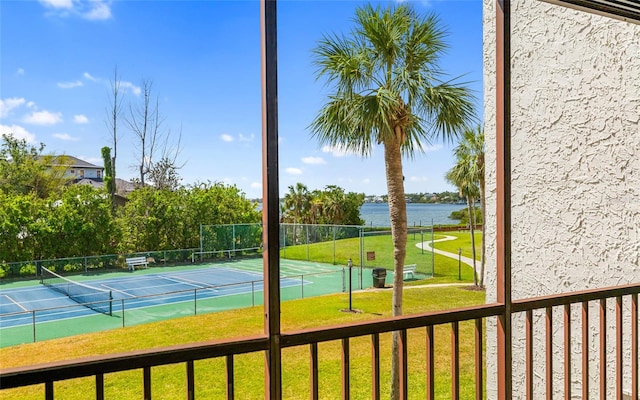 view of tennis court featuring a yard, fence, and a water view