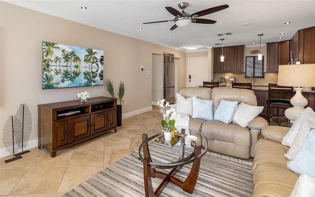 living area featuring baseboards, light tile patterned floors, visible vents, ceiling fan, and crown molding