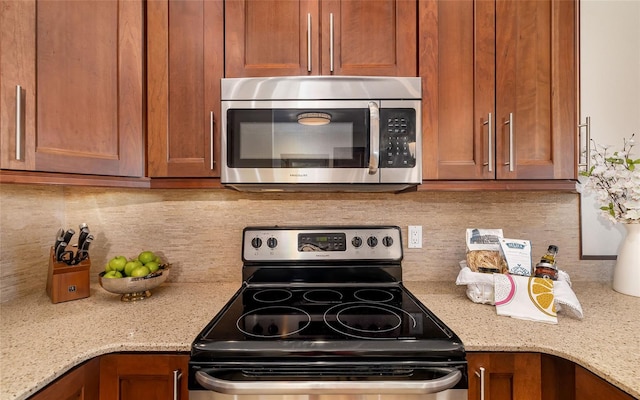 kitchen featuring brown cabinetry, stainless steel appliances, backsplash, and light stone counters