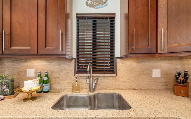 kitchen featuring backsplash, light stone countertops, brown cabinetry, and a sink