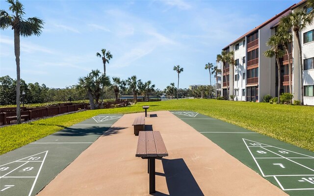 view of community with shuffleboard, fence, and a lawn