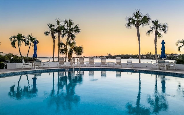 pool at dusk with a patio area and a community pool