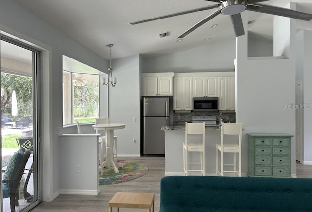 kitchen with a ceiling fan, stainless steel appliances, white cabinetry, decorative backsplash, and vaulted ceiling