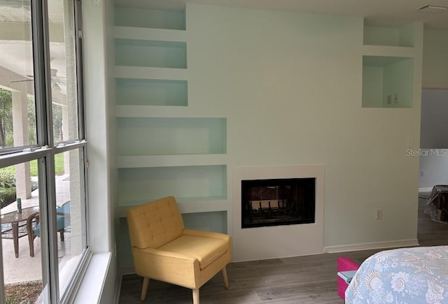 bedroom with multiple windows, a multi sided fireplace, wood finished floors, and baseboards