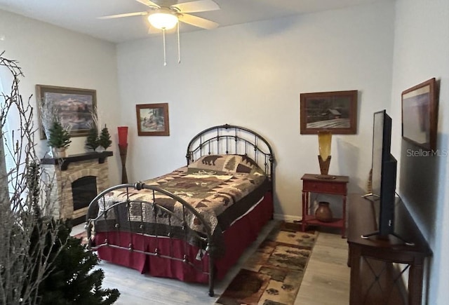 bedroom with a fireplace, ceiling fan, and wood finished floors