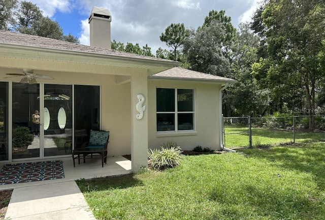 rear view of property featuring a lawn, fence, ceiling fan, a patio area, and stucco siding