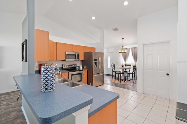kitchen featuring stainless steel appliances, a peninsula, light tile patterned floors, dark countertops, and a sink