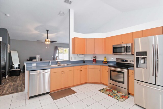 kitchen with stainless steel appliances, a sink, dark countertops, light brown cabinets, and a peninsula