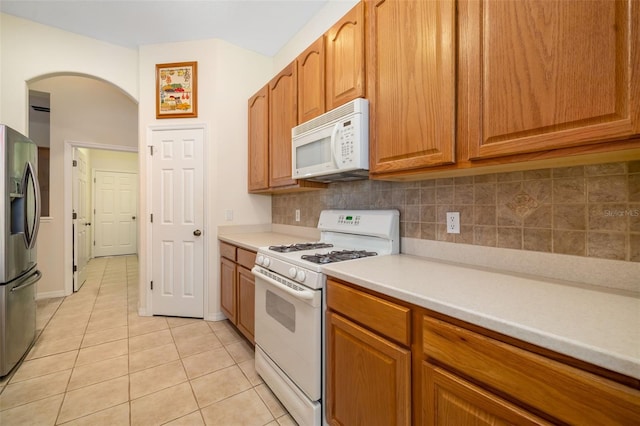 kitchen with white appliances, arched walkways, light tile patterned flooring, tasteful backsplash, and light countertops