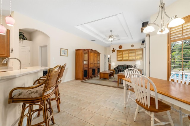 dining space with a raised ceiling, light tile patterned floors, a ceiling fan, arched walkways, and baseboards