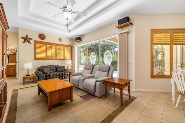 living room with light tile patterned floors, a ceiling fan, baseboards, and a tray ceiling