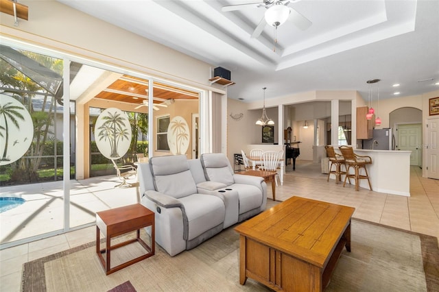 living area featuring a ceiling fan, light tile patterned floors, arched walkways, and a raised ceiling
