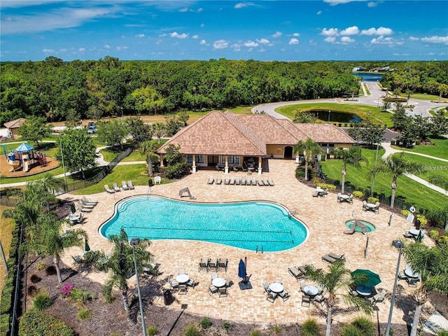 community pool with fence, a patio, and a forest view