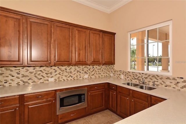 kitchen featuring stainless steel microwave, a sink, ornamental molding, tasteful backsplash, and light countertops