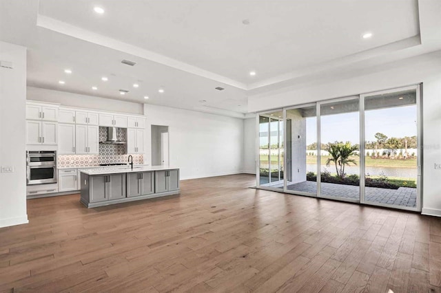 17927 Palmiste Dr, Bradenton, FL 34202 - kitchen with wall chimney exhaust hood, a tray ceiling, double oven, wood finished floors, and recessed lighting