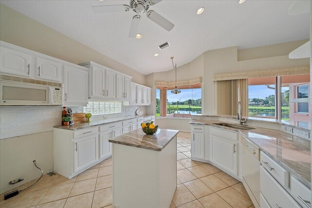 kitchen featuring light stone countertops, a center island, white appliances, a sink, and vaulted ceiling