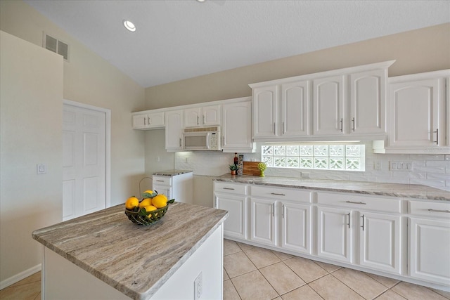 kitchen featuring white cabinets, visible vents, tasteful backsplash, white microwave, and light stone counters