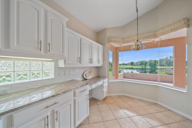 kitchen with white cabinets, light stone counters, baseboards, decorative light fixtures, and tasteful backsplash