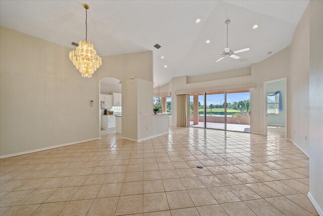 empty room with ceiling fan with notable chandelier, high vaulted ceiling, arched walkways, light tile patterned floors, and baseboards