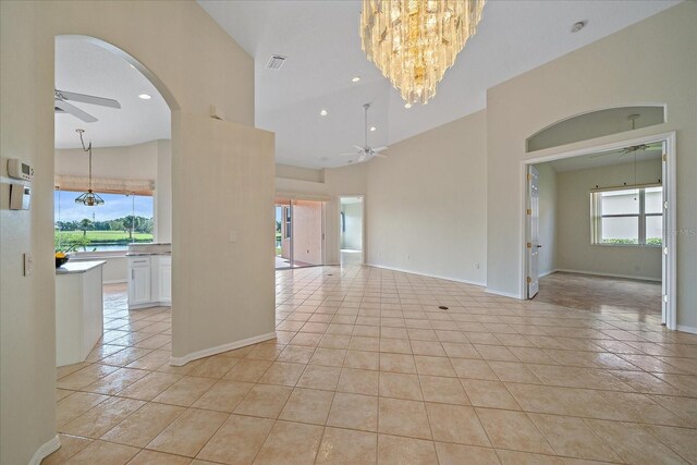 empty room with a towering ceiling, baseboards, light tile patterned flooring, and ceiling fan with notable chandelier