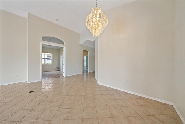 spare room featuring baseboards, light tile patterned floors, ceiling fan with notable chandelier, a towering ceiling, and arched walkways