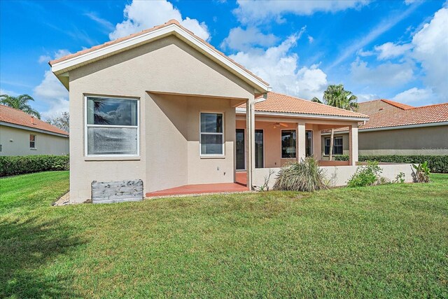 back of property featuring stucco siding, a tile roof, a lawn, and ceiling fan