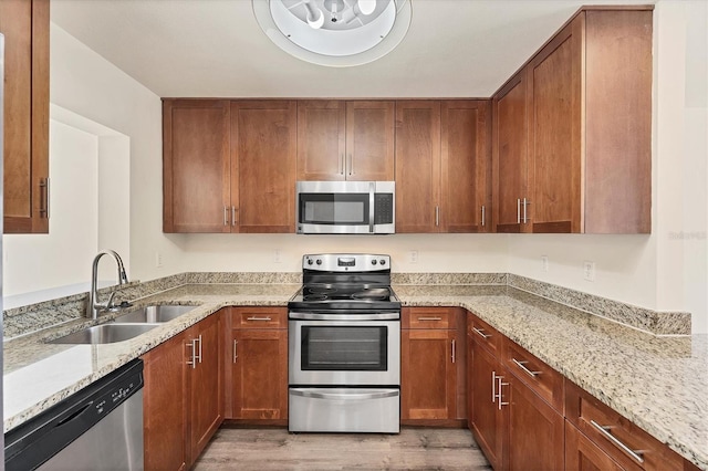 4907 4th Avenue Cir NW, Bradenton, FL 34209 - kitchen featuring light wood-style flooring, a sink, brown cabinetry, appliances with stainless steel finishes, and light stone counters
