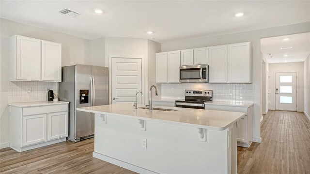 kitchen featuring visible vents, a sink, a center island with sink, stainless steel appliances, and tasteful backsplash