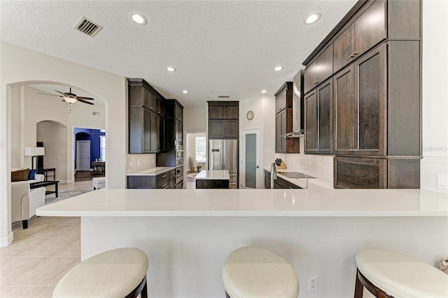 8103 Snowy Egret Pl, Bradenton, FL 34202 - kitchen with arched walkways, wall chimney range hood, dark brown cabinets, light countertops, and ceiling fan