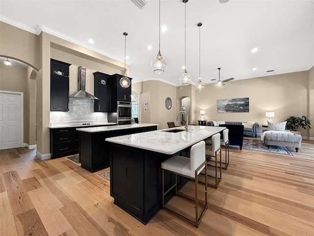 6567 Eagle Ridge Way, Lakeland, FL 33813 - kitchen featuring arched walkways, an island with sink, dark cabinets, wall chimney range hood, and ornamental molding
