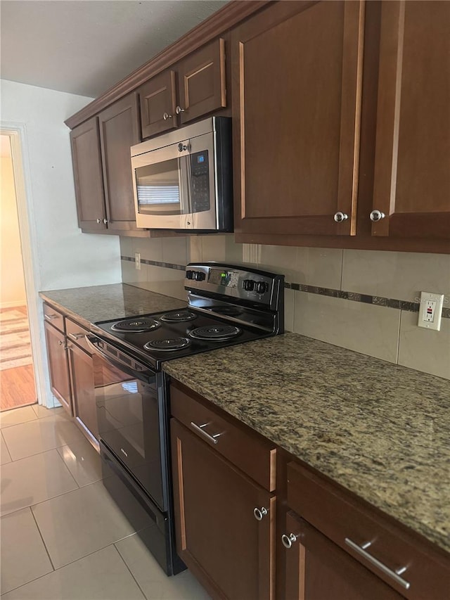 kitchen with light tile patterned floors, dark stone counters, black range with electric stovetop, stainless steel microwave, and tasteful backsplash
