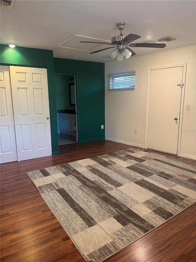 unfurnished living room featuring a ceiling fan, attic access, baseboards, visible vents, and wood finished floors