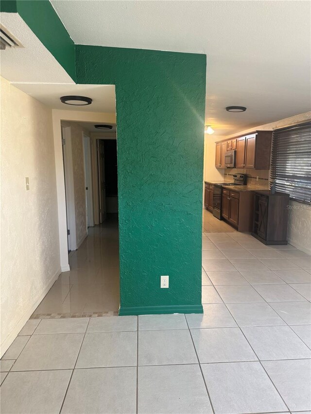 unfurnished room with light tile patterned flooring, a textured wall, and visible vents
