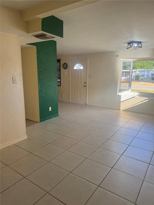empty room with light tile patterned floors, baseboards, visible vents, and a textured wall