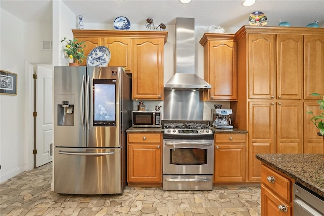 kitchen with brown cabinetry, visible vents, dark stone countertops, wall chimney range hood, and appliances with stainless steel finishes